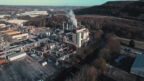 Aerial view of industrial complex with smoke rising. Buildings and pipes form Stock Footage 345669045