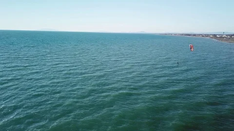Aerial view of A Kite surfer sails in front of a sand beach in a sunny windy day Stock Footage 106538744