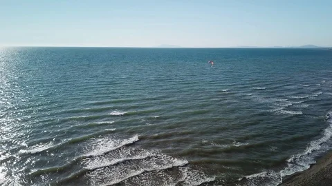 Aerial view of A Kite surfer sails in front of a sand beach in a sunny windy day Stock Footage 106539891