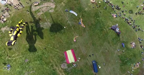 Aerial view of kites with shadow and Tourists on green meadow at Kite Festival Stock Footage