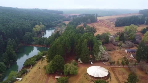 Aerial view of a lake surrounded by dense forest and farmland with a large tent Stock Footage 308979018