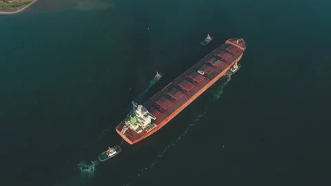 Aerial view of a large cargo ship being driven out of the harbor by four Stock Footage 157653794