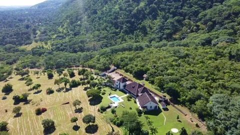 Aerial view of a large house with a pool surrounded by trees and a forest on a Stock Footage 313318599