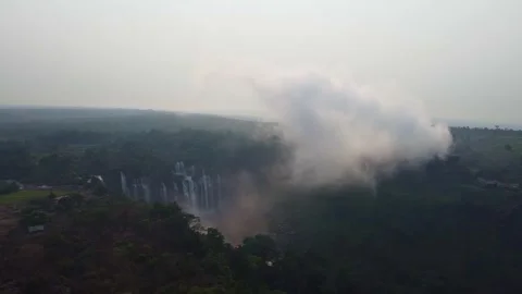 Aerial view of a large waterfall cascading down a cliff surrounded by lush green Stock Footage 307889695