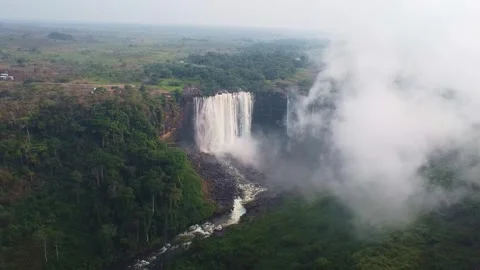 Aerial view of a large waterfall cascading down a cliff surrounded by dense Stock Footage 307890134