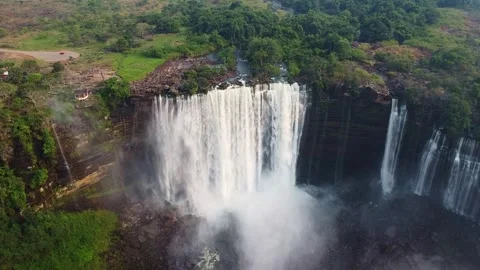 Aerial view of a large waterfall cascading over a cliff surrounded by lush green Stock Footage 307890730