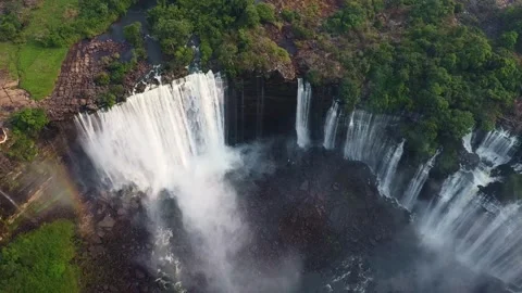 Aerial view of a large waterfall cascading down a rocky cliff surrounded by lush Stock Footage 307890908