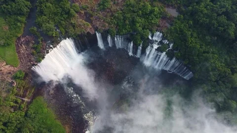 Aerial view of a large waterfall cascading down a cliff surrounded by lush green Stock Footage 307891169