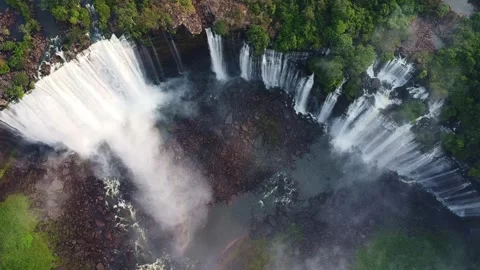 Aerial view of a large waterfall cascading over rocks surrounded by lush green Stock Footage 307891899