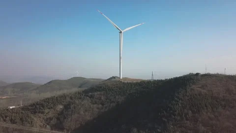 Aerial View of Large White Wind Turbine on Green Hilltop Under Clear Blue Sky Vidéo 334863361