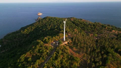 Aerial view of a large wind turbine on a hill among palm trees against the Stock Footage 243353950