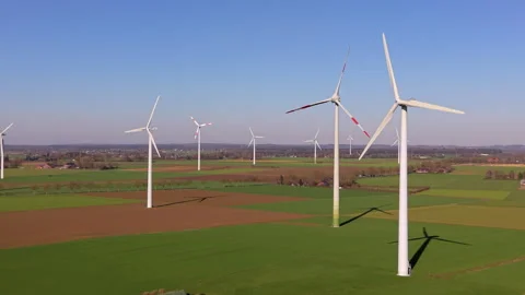 Aerial view of large wind turbines across green agricultural fields under c.. Stockbeeldmateriaal 336926069