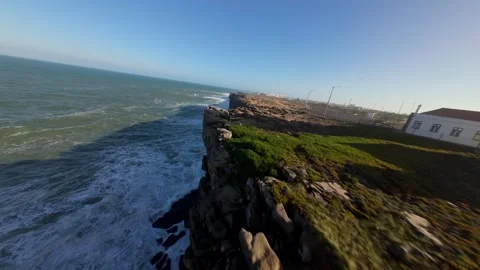 Aerial view of lighthouse on cliffside, turbulent sea below, golden hour light Video stock 346077169