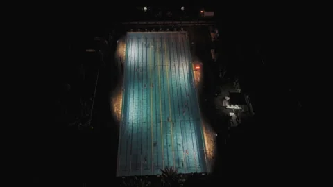 Aerial view of a lit Olympic pool in Bali at night with swimmers and lamps Stock Footage 326540466