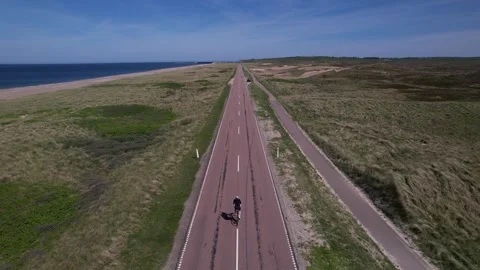 Aerial View of Lone Cyclist Riding Along Straight Coastal Road in Denmark Stock Footage 343533387