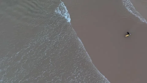 Aerial view of a lone surfer riding the waves on a serene beach during sunset Stock Footage 283390464