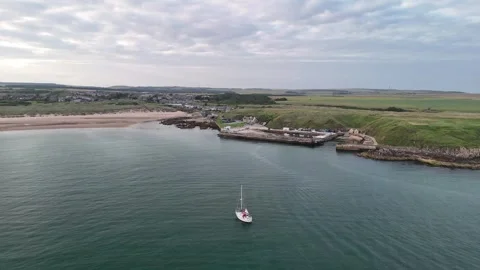 Aerial view of a lonely sailboat anchored in the turquoise waters of Cruden Bay Stock Footage 330675615