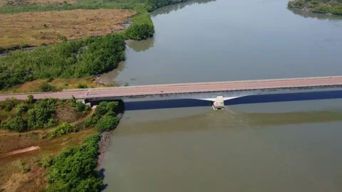 Aerial view of a long bridge spanning a wide river with lush green vegetation on Stock Footage 317449841