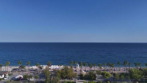 Aerial view of a long coast with beach umbrellas and palm trees by turquoise sea Stock Footage 344356393