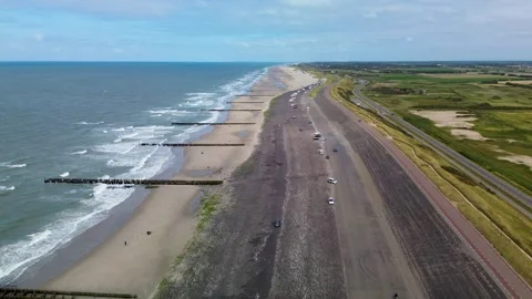Aerial view of a long sandy beach with ocean waves, breakwaters, parked cars Stock-Footage 316783350