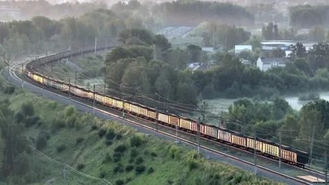 Aerial view. A long train with many cars rides in the rays of dawn. Video stock 234542062