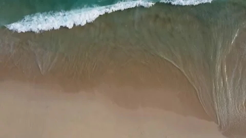 Aerial view looking straight down onto crashing waves hitting a golden beach Stock-Footage 229785890