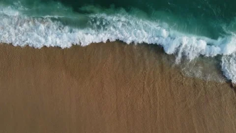 Aerial view looking straight down onto crashing waves hitting a golden beach Stock-Footage 229789894