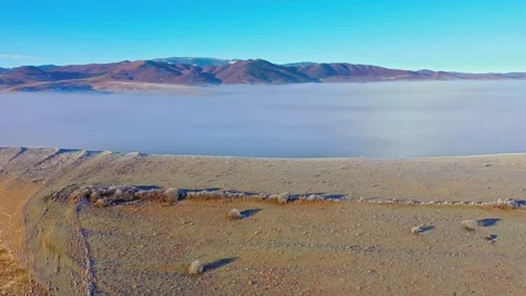 Aerial view of low fog rolling over a mountain lake in early morning Stock Footage 345484586