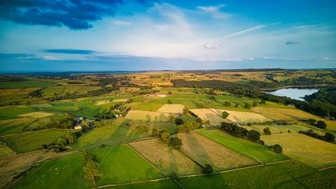 Aerial view of a lush countryside with patchwork fields, trees, and a lake .. Stock Photos