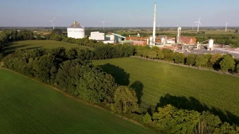 Aerial view of lush green fields, a river, and an industrial plant with tall Видео 315338037