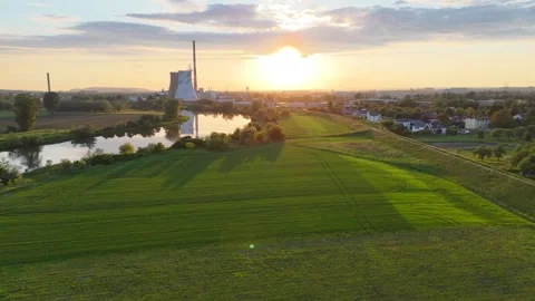Aerial view of lush green fields and a river at sunset, with a power plant Видео 335478341