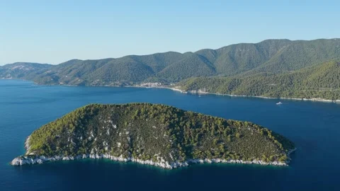 Aerial view of a lush, green, forested island surrounded by deep blue sea, with Stock Footage 346704524