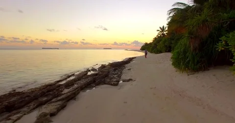 Aerial view of a man being chased, running away from and ducking a drone on a be Stock Footage