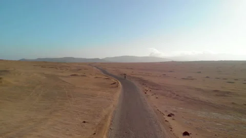 Aerial view of man biking on road through dry desert landscape Stock Footage