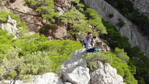 Aerial view man with camera sits on mountain crest top Video stock 103836040