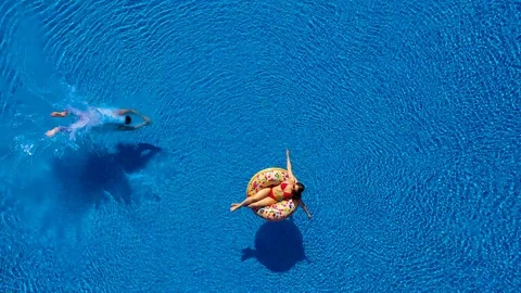 Aerial view of man dives into the the pool while girl is lying on a donut pool Stock Footage 110813318