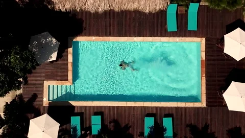 Aerial view of a man dives into the pool and swims under the water at sunset Stock Footage 142766361