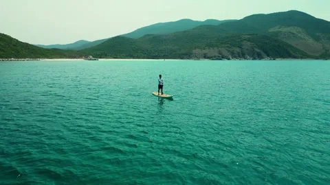 Aerial view of a man with an oar on a for sup board in the sea on the mountains Stock Footage 241446767