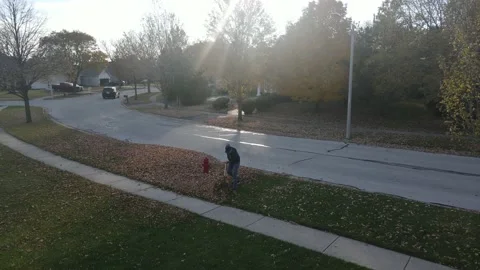 Aerial view of a man raking up fallen autumn leaves on a suburban street. Stock Footage 143749537