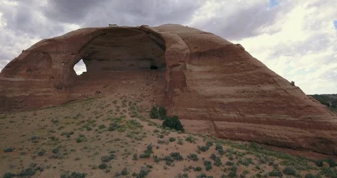 Aerial view of man rappelling within sandstone arch with stormy skies Stock Footage 111406336