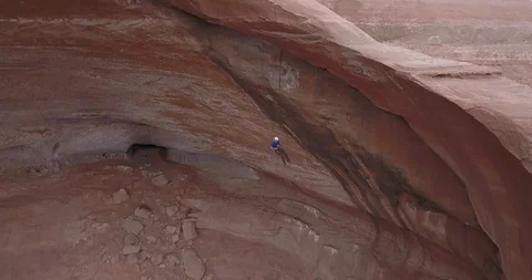 Aerial view of man rappelling/abseiling within a huge stone arch Stock Footage 111406562