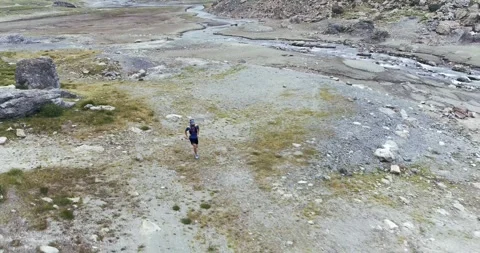 Aerial view of man running alone in a rocky mountain flat land. River flowing Видео 153481840
