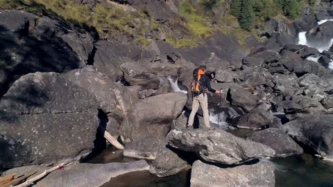 Aerial view of man standing in front of a waterfall river with rocks, trees Stock Footage 82289444