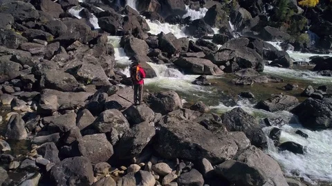 Aerial view of man standing in front of a waterfall river with rocks, river Stock Footage 82411465