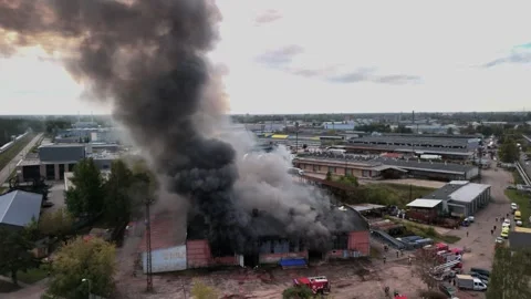 Aerial view of massive industrial fire with thick black smoke and fire trucks Stock Footage 321361890