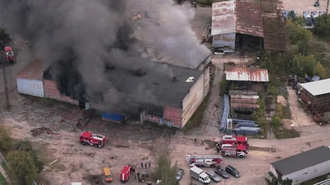 Aerial view of massive industrial fire with thick black smoke and fire trucks Stock Footage 321361919