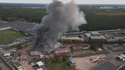 Aerial view of massive industrial fire with thick black smoke and fire trucks Stock Footage 321362013