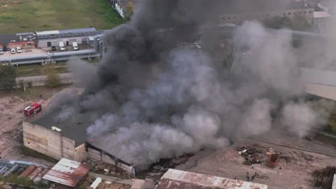 Aerial view of massive industrial fire with thick black smoke and fire trucks Stock Footage 321362133