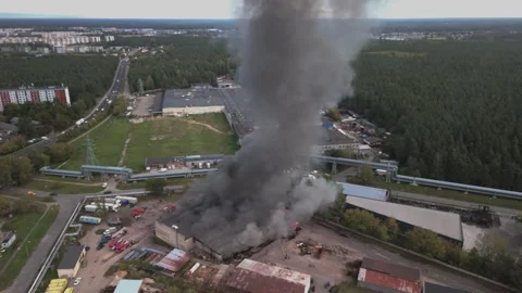 Aerial view of massive industrial fire with thick black smoke and fire trucks Stock Footage 321362388