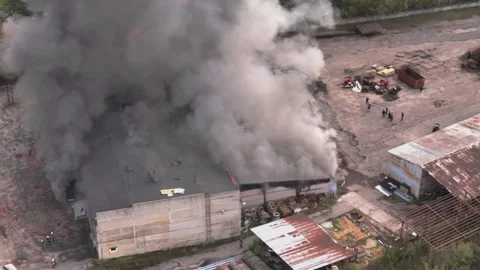 Aerial view of massive industrial fire with thick black smoke and fire trucks Stock Footage 321362471